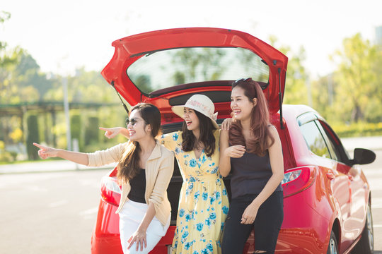 Enjoying woman with her girlfriend traveler sitting on hatchback red car. summer vacation, holidays, travel, road trip and people concept .