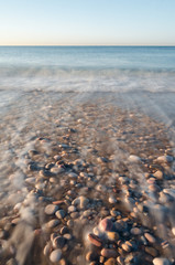 Orilla de la playa con piedras al amanecer agua en movimiento