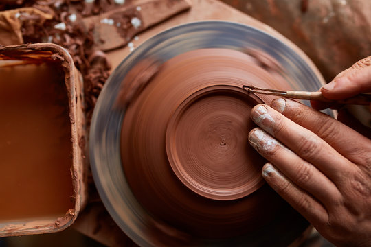 Adult male potter master modeling the clay plate on potter's wheel. Top view, closeup, hands only.