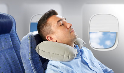 travel, comfort and people concept - man sleeping in plane with inflatable cervical neck pillow...