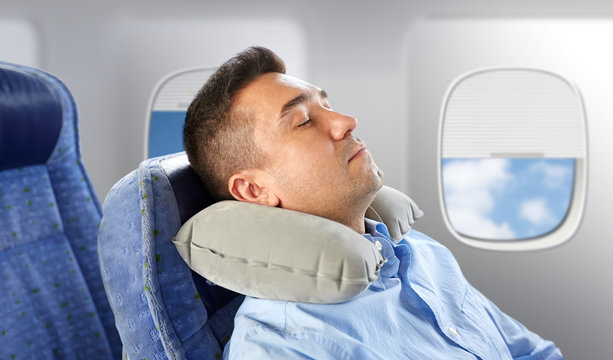 Travel, Comfort And People Concept - Man Sleeping In Plane With Inflatable Cervical Neck Pillow Over Porthole Background