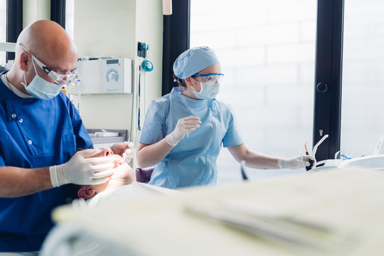 Dentist and dental nurse carrying out dental procedure on male patient, close-up