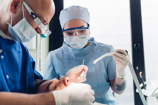 Dentist and dental nurse carrying out dental procedure on male patient, close-up