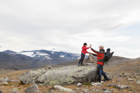 Man with sons high fiving over cairn in mountain landscape, Jotunheimen National Park, Lom, Oppland, Norway