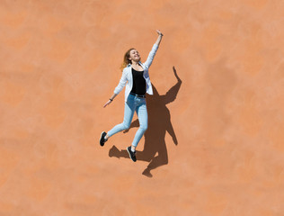 Joyful happy young woman jumping against orange wall in sunny day