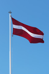 Flag of Latvia waving against blue sky.