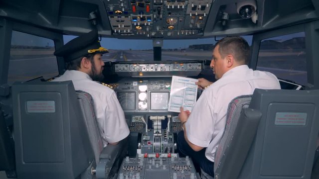 Pilots read a manual in a cockpit of a flight simulator. 4K.