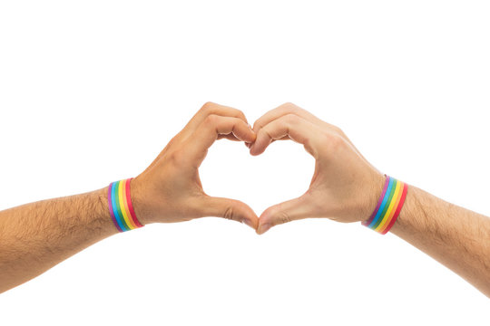 lgbt, same-sex love and homosexual relationships concept - close up of male couple hands with gay pride rainbow awareness wristbands showing heart gesture