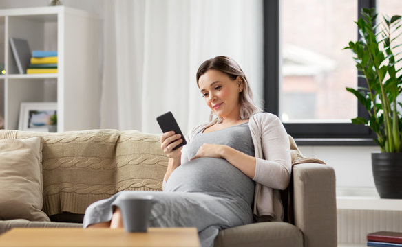pregnancy, people and technology concept - happy pregnant woman with smartphone at home