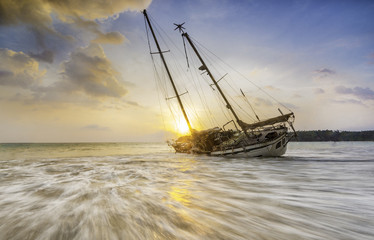 Damaged sailing boat,shipwreck on the coast on sunset