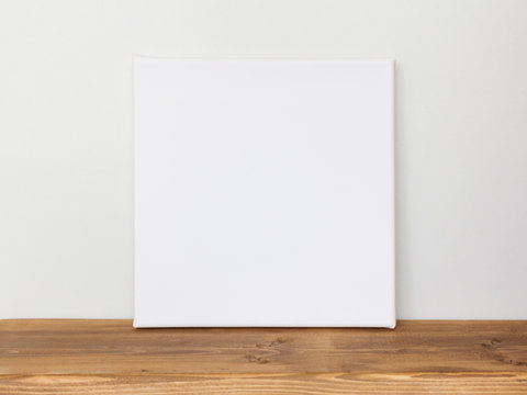 Blank square canvas leaning against a gray wall.