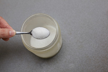 man's hand hold a spoon full of sugar.