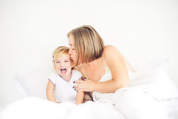 Obraz na płótnie Canvas Happy and loving mother having fun and kissing her daughter on the bed. Family morning concept. Spending free time together at home. Soft selective focus. Space for text.