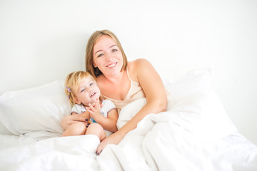 Obraz na płótnie Canvas Happy and loving mother having fun and embrace her daughter on the bed. Family morning concept. Spending free time together at home. Soft selective focus. Space for text.