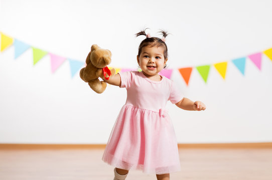 childhood, people and celebration concept - happy baby girl with teddy bear toy on birthday party