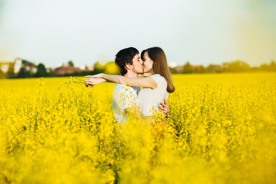Young couple in love embrace each other and have passionate kiss while pose against yellow field of flowers, demonstrate truthful relationships and devotion. People, love and devotion concept