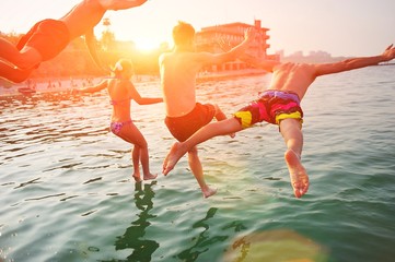 Group of happy people having fun jumping in the sea water from a pier. Friends in mid air on a...