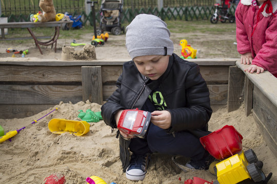 The Child Is Playing In The Sandbox With Toys