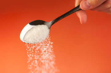 sugar is poured out from a spoon which is held by a hand on an orange red background