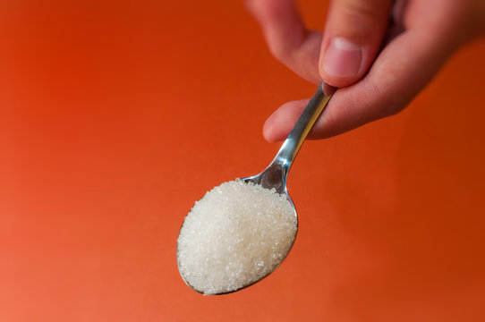 sugar in a spoon which is held by a hand on an orange red background