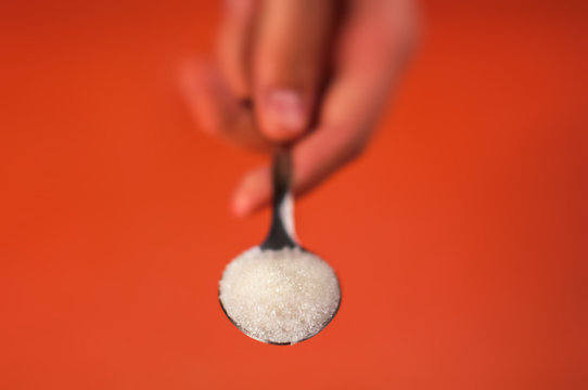 sugar in a spoon which is held by a hand on an orange red background