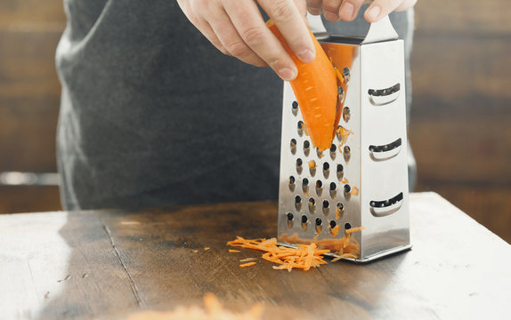 Close up male hands rubs carrots on grater