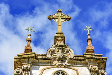 Fototapeta na wymiar Baroque style crucifix and others ornaments on top of ancient and historical church in the city of Ouro Preto in Minas Gerais