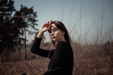 A girl stands in a field in the sun in a black sweater close-up portrait