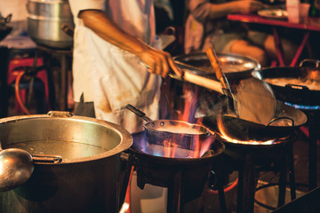 Street food chef cooking meat and fish in a pan with fire and flames under it. Chinatown, Bangkok,...