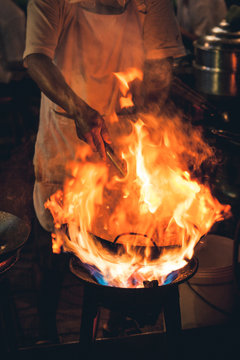 Street food chef cooking meat and fish in a pan with fire and flames under it. Chinatown, Bangkok, Thailand