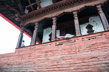 A man is asleep on the railing of the porch of the old church. Streets Takmandu early in the morning are full of people who are preparing for a day's work. People sleep on the street. Nepal. Central s