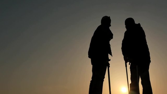 elder man gives helping hand to cripple and he thanks him silhouettes follow focus