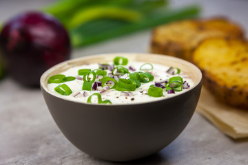 Bowl with curd decorated with spring onion. Baked jacket potatoes and spring onion on the background