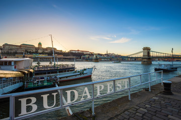 Obraz premium Budapest, Hungary - Boats on River Danube with Buda Castle Royal Palace and Szechenyi Chain Bridge at sunset with clear blue sky