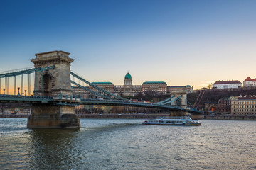 Fototapeta na wymiar Budapest, Hungary - Beautiful Szechenyi Chain Bridge with sightseeing boat on River Danube and Buda Castle Royal Palace at blue hour with clear blue sky