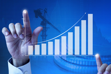 Close up of a businessman’s hands expanding an exponential line curve and bar chart on blue...