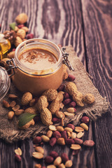 Natural peanut butter with oil in a glass jar and peanuts