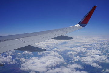 Obraz premium Part of the wing of a plane high in the blue sky among white clouds.