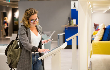 Woman with phone configuring furniture at the self-service device in the store