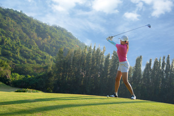 Asian woman golf player doing golf swing tee off on the green evening time, she presumably does exercise. Healthy and Lifestyle Concept.