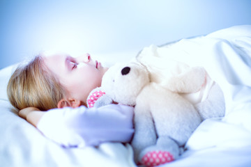 Child little girl sleeps in the bed with a toy teddy bear