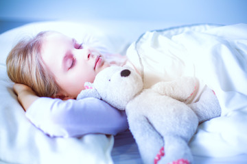 Child little girl sleeps in the bed with a toy teddy bear