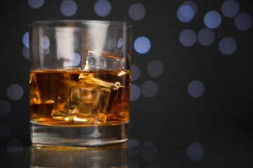 Whiskey in a glass with ice on a dark background with a bokeh