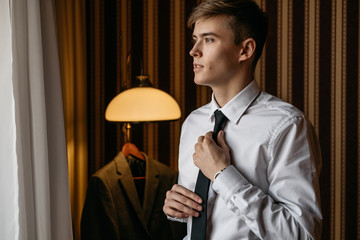 A handsome, young man binds his tie