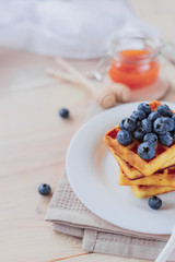 Belgian waffles with blueberries on the light wooden table. Healthy breakfast. 