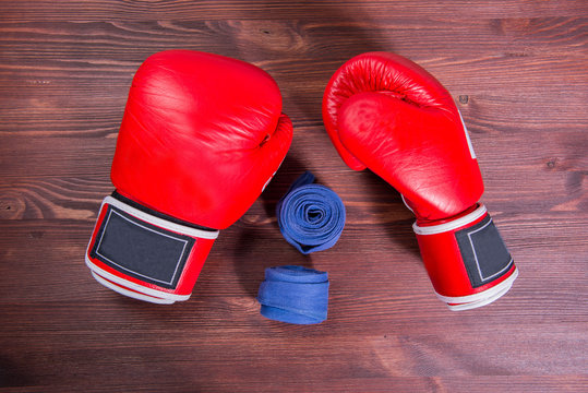 Red boxing gloves and bandage on wooden brown background. Top view.