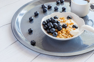 Healthy breakfast of granola with blueberries and yogurt and cup of coffee on a tray