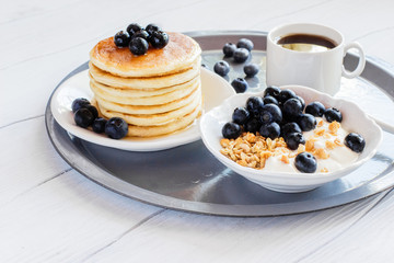 Healthy breakfast of granola with blueberries and yogurt and pancakes on a tray
