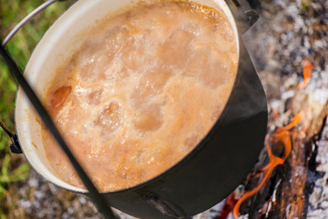 Boiling, hot goulash soup with meat, paprika, potatoes, onion, carrots is the traditional dish of Hungarian cuisine. Meat stew being prepared in crock pot on open fire. Picnic at the weekend in nature