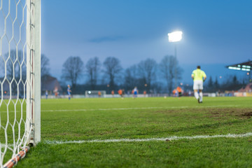 Detail of the post and net of the football goal in the background players in action.